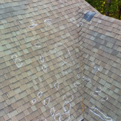 Marked shingle roof showing signs of hail damage with chalk circles indicating impact points.
