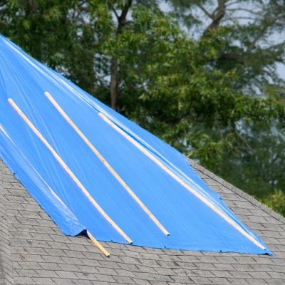 A residential roof covered with a blue tarp secured with wooden battens, protecting it from rain during a repair or replacement.