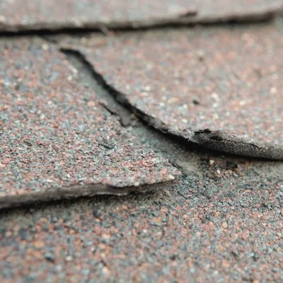 Close-up of damaged asphalt shingles curling on a roof.