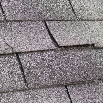 Close-up view of worn and damaged asphalt shingles with visible curling and granule loss.