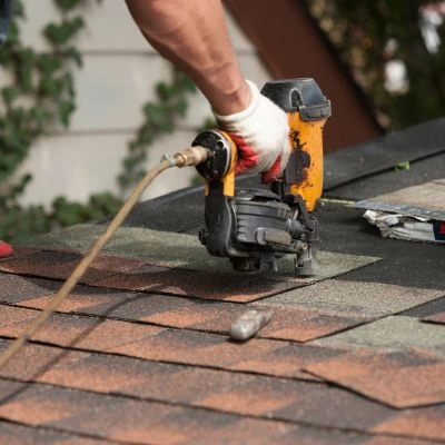 Roofer using a pneumatic nail gun to install new asphalt shingles during a roof repair project in Brooksville