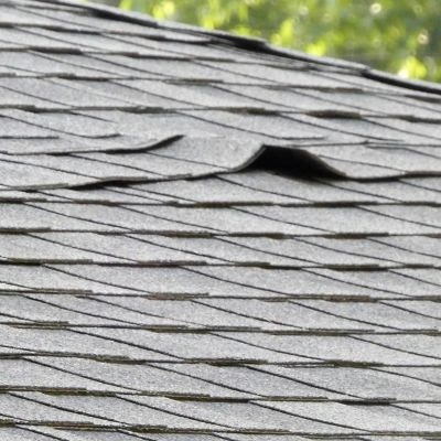 Close-up of damaged asphalt shingles with a raised curling section that could allow water penetration.