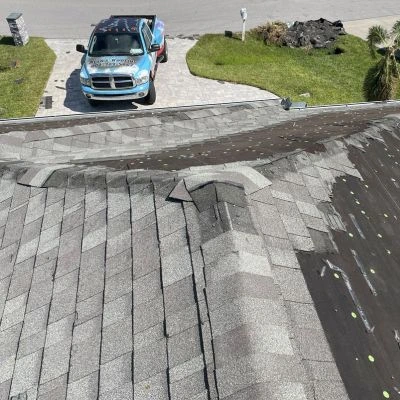View of a roof with missing shingles and an Alan's Roofing truck in the driveway.