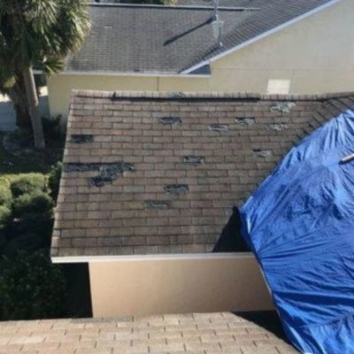 storm damaged roof with a blue tarp covering a section of the damage