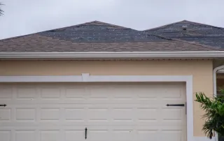 Storm-damaged asphalt shingle roof on a Florida home showing missing shingles and exposed underlayment beneath overcast skies