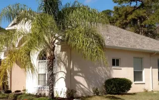 A Florida home with an asphalt shingle roof surrounded by palm trees and lush landscaping.